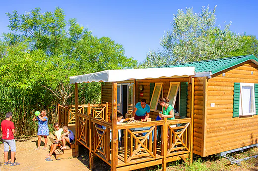 Famille profitant de la terrasse d'un Mobil-home en bois au camping CAPFUN La Nina � Agde (34).
